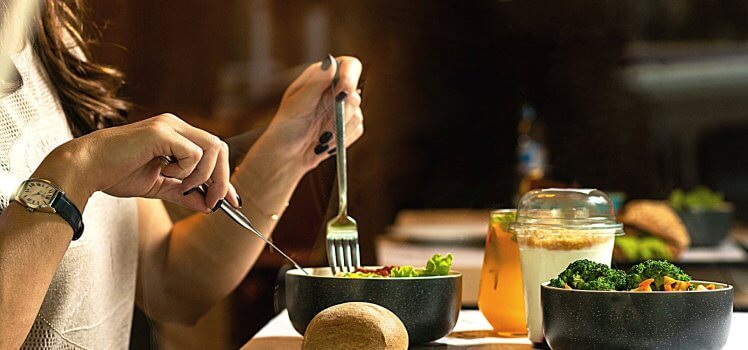 Closeup profile view of a person eating a salad on a table.