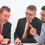 Three men having a healthy debate sitting at a table looking at a paper.