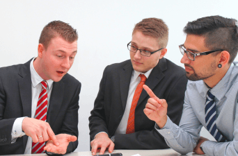 Three men having a healthy debate sitting at a table looking at a paper.