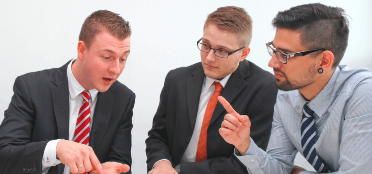 Three men having a healthy debate sitting at a table looking at a paper.