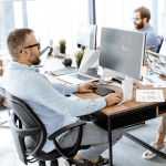 Group of four people sitting at a large table independently working.