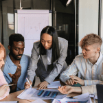 Group of employees sitting closely at a conference table marking a graphic sheet.