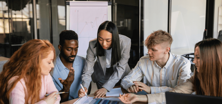 Group of employees sitting closely at a conference table marking a graphic sheet.