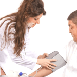 Woman in a white coat applying a blood pressure cuff to a middle aged man.