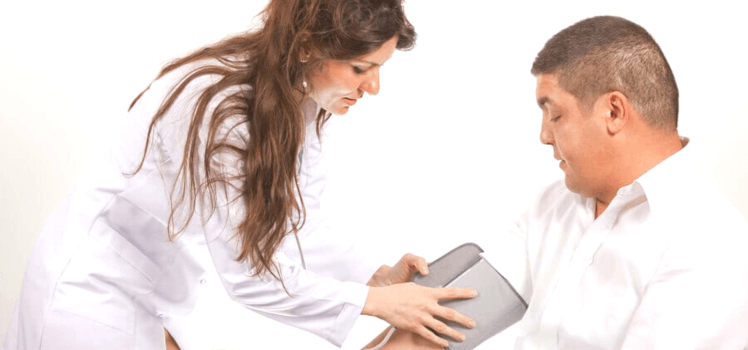 Woman in a white coat applying a blood pressure cuff to a middle aged man.