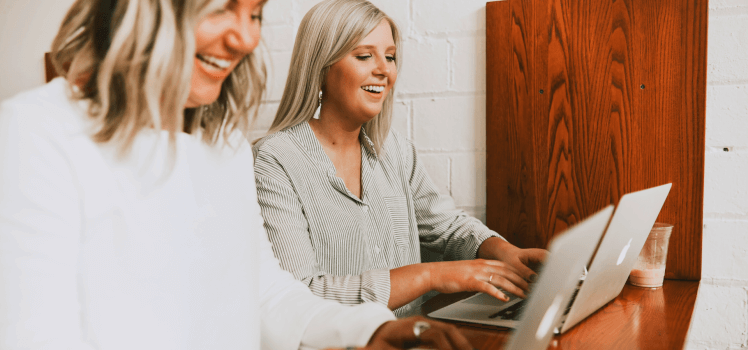 Two women sitting at a small table working on laptops.