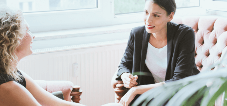 Two women sitting closely having a conversation in a sunlight filled room.