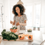 Woman in a bright dining room making a salad in an orange salad bowl.
