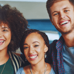 Three young people shoulder to shoulder smiling.