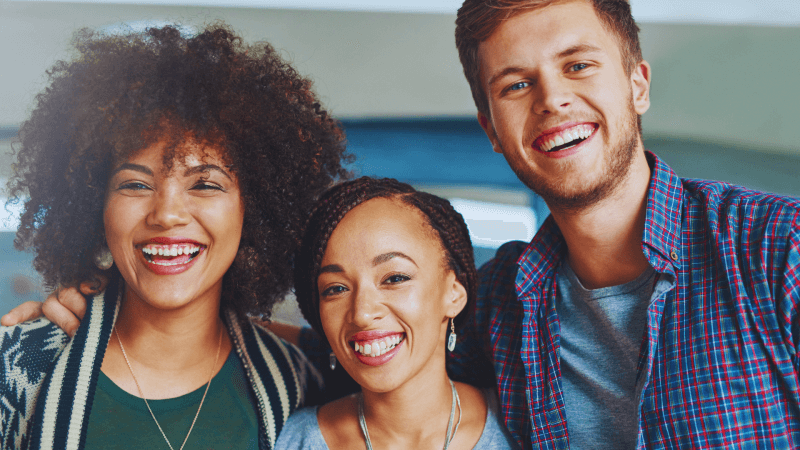 Three young people shoulder to shoulder smiling.