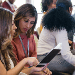 Two women conversing and looking at a pamphlet in a large group.