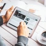 Man with a beard working from a tablet with a cup of coffee.