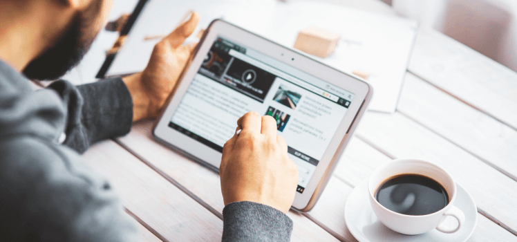 Man with a beard working from a tablet with a cup of coffee.