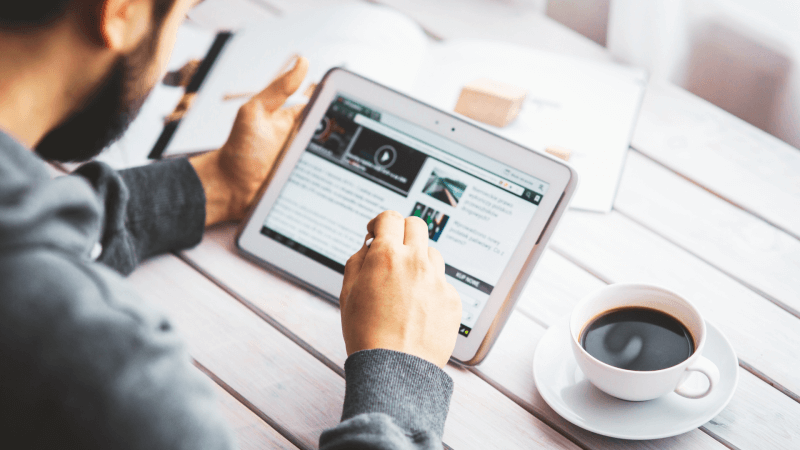 Man with a beard working from a tablet with a cup of coffee.