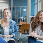 Two women and a man sitting in chairs in an office setting laughing.