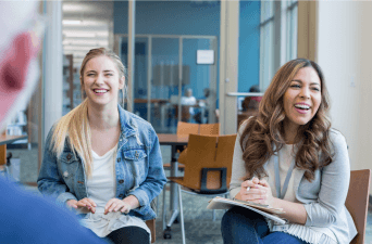 Two women and a man sitting in chairs in an office setting laughing.