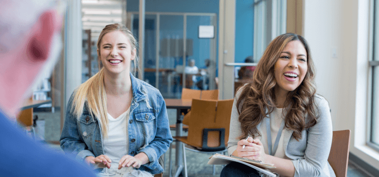 Two women and a man sitting in chairs in an office setting laughing.