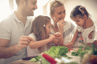 family preparing a salad together and laughing.