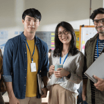 Group of four young corporate workers standing in a row smiling.