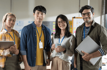 Group of four young corporate workers standing in a row smiling.