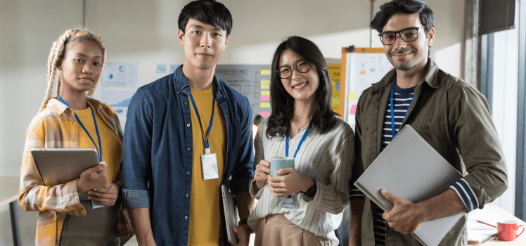 Group of four young corporate workers standing in a row smiling.