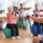 Exercise class with individuals sitting on exercise balls holding dumbbells.