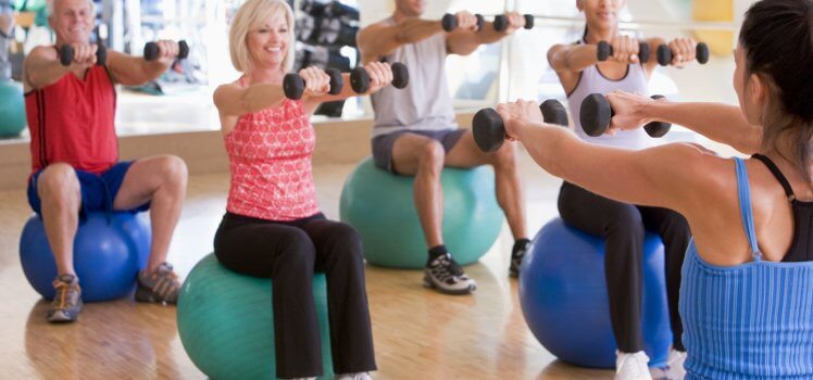 Exercise class with individuals sitting on exercise balls holding dumbbells.