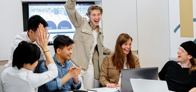 Six employees in a conference celebrating a milestone and laughing.