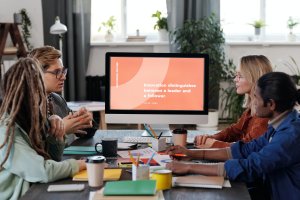 Diverse group of four employees viewing a presentation on a desktop screen at a conference table.