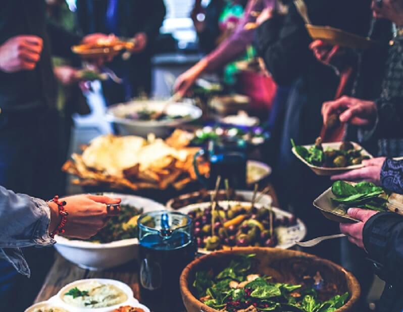 table of food with people gathered around for company potluck