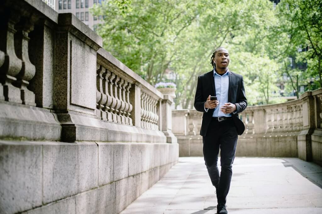 African American Male taking a meeting from his phone as he walks briskly in the city.