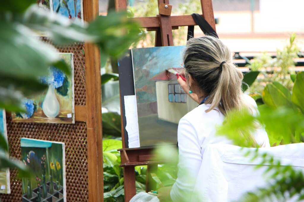 Blonde woman painting a canvas outside during a painting class. 
