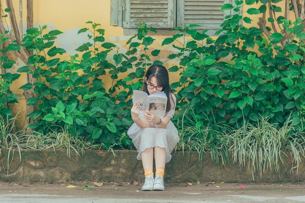 Woman sitting on a curb reading outside. 