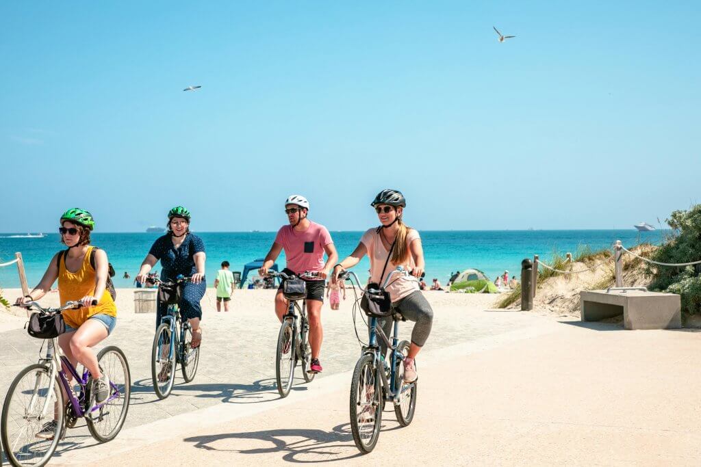 Four individuals in bike helmets biking on the beach.
