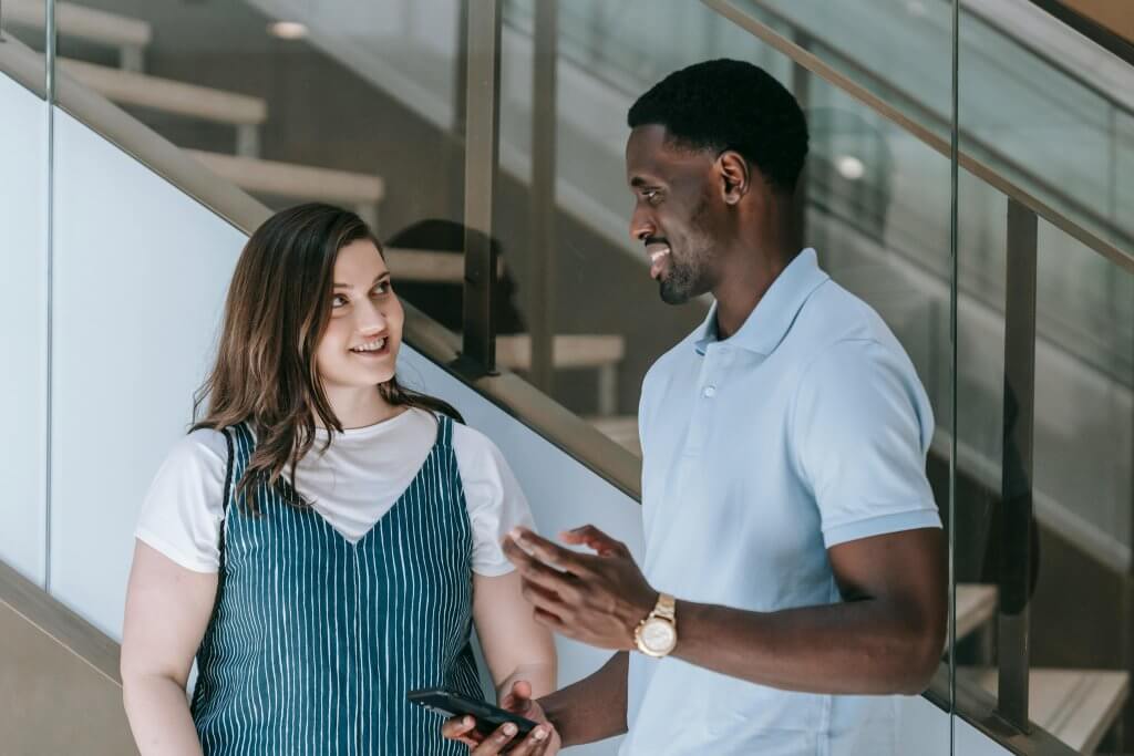 A male and female worker standing in a hallway talking as they build connections through wellness at work.