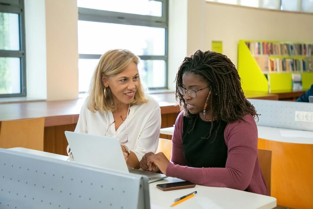 Library teacher who is in the employee wellness program assisting a student at a table.