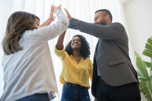 Group of three employees giving a high-five in celebration of a milestone for employee commitment. Employee wellness programs are a strategic investment. When employees feel supported, they are more likely to stay committed to their roles.