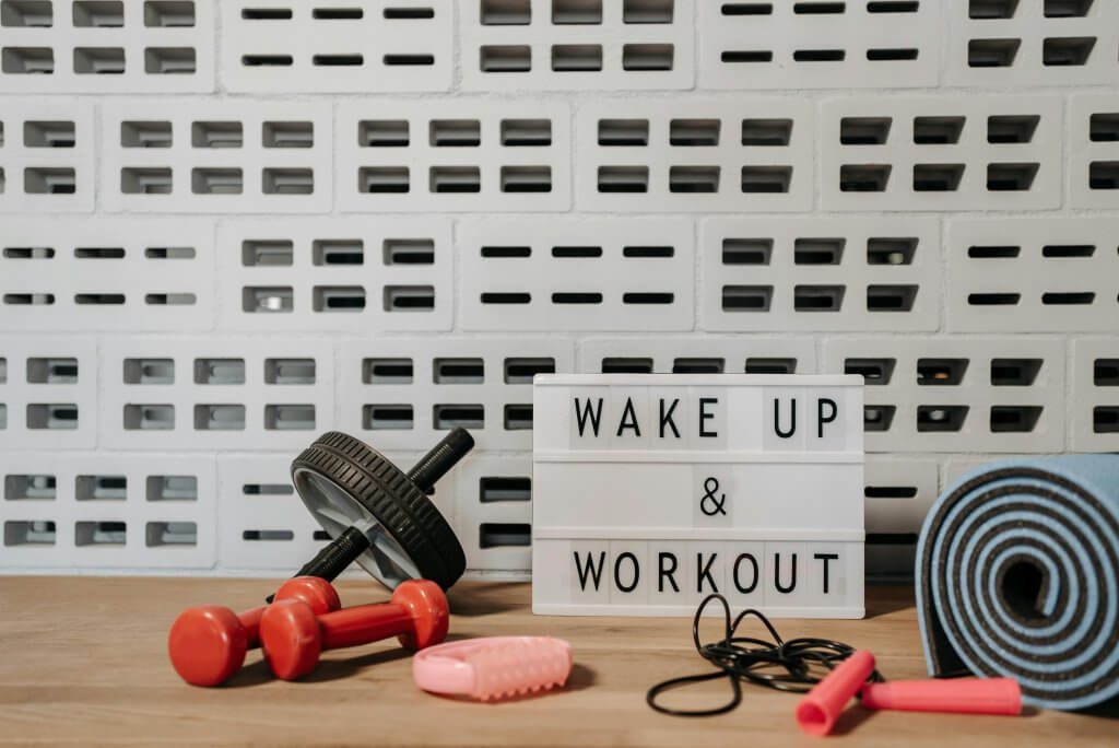 Sign saying "wake up & workout" surrounded by workout gear to remind people to prioritize wellness while at work.