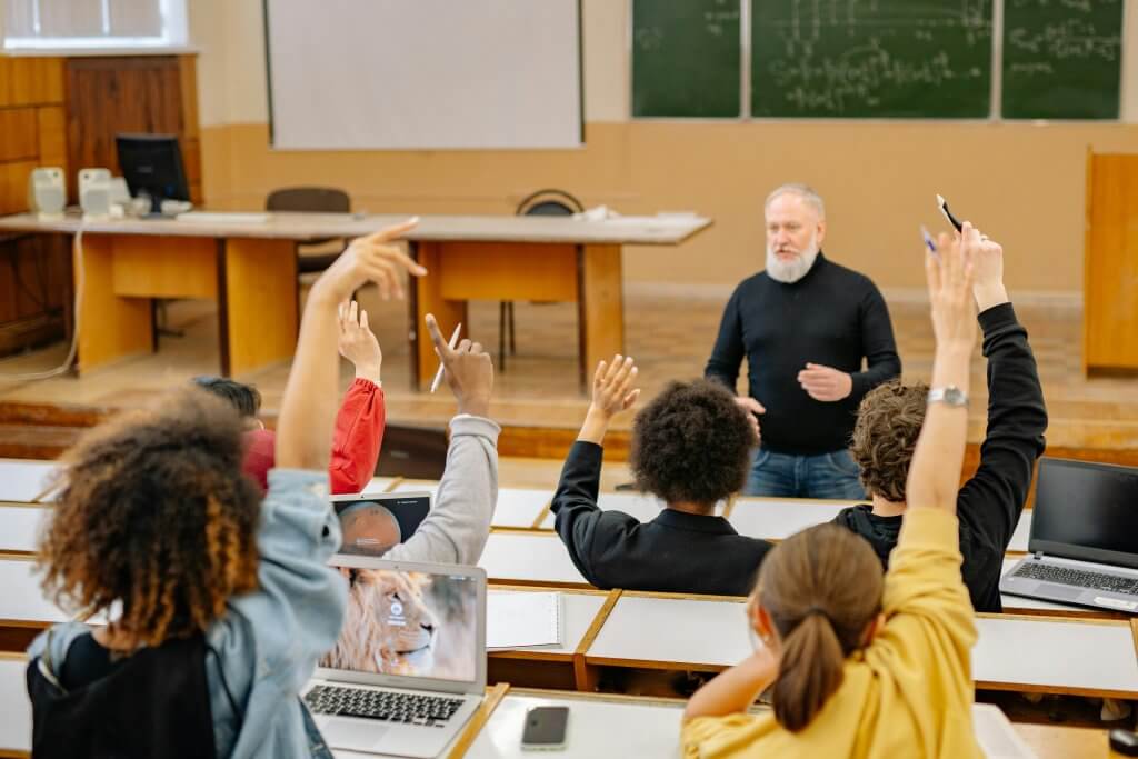 Professor in the school wellness program teaching in the front of a large class full of raised hands.