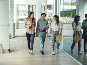 Three colleagues walking down a corridor discussing the importance for exercise movement at work. Organizations that prioritize physical, emotional, and mental well-being are more likely to see a return on investment through improved employee engagement, retention, and overall productivity.