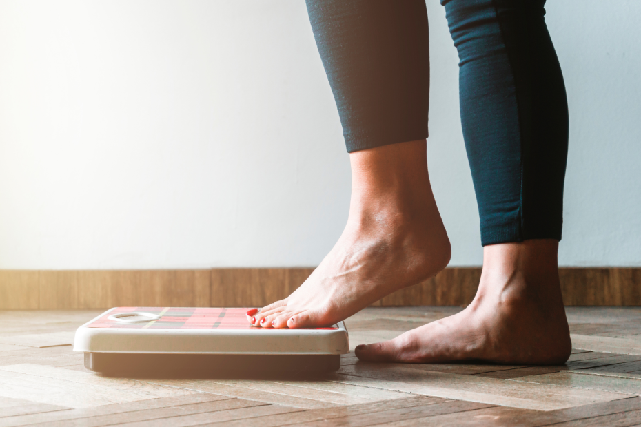 Person stepping onto a scale to track progress, illustrating how measuring outcomes and engagement is essential for identifying gaps in a workplace wellness program.